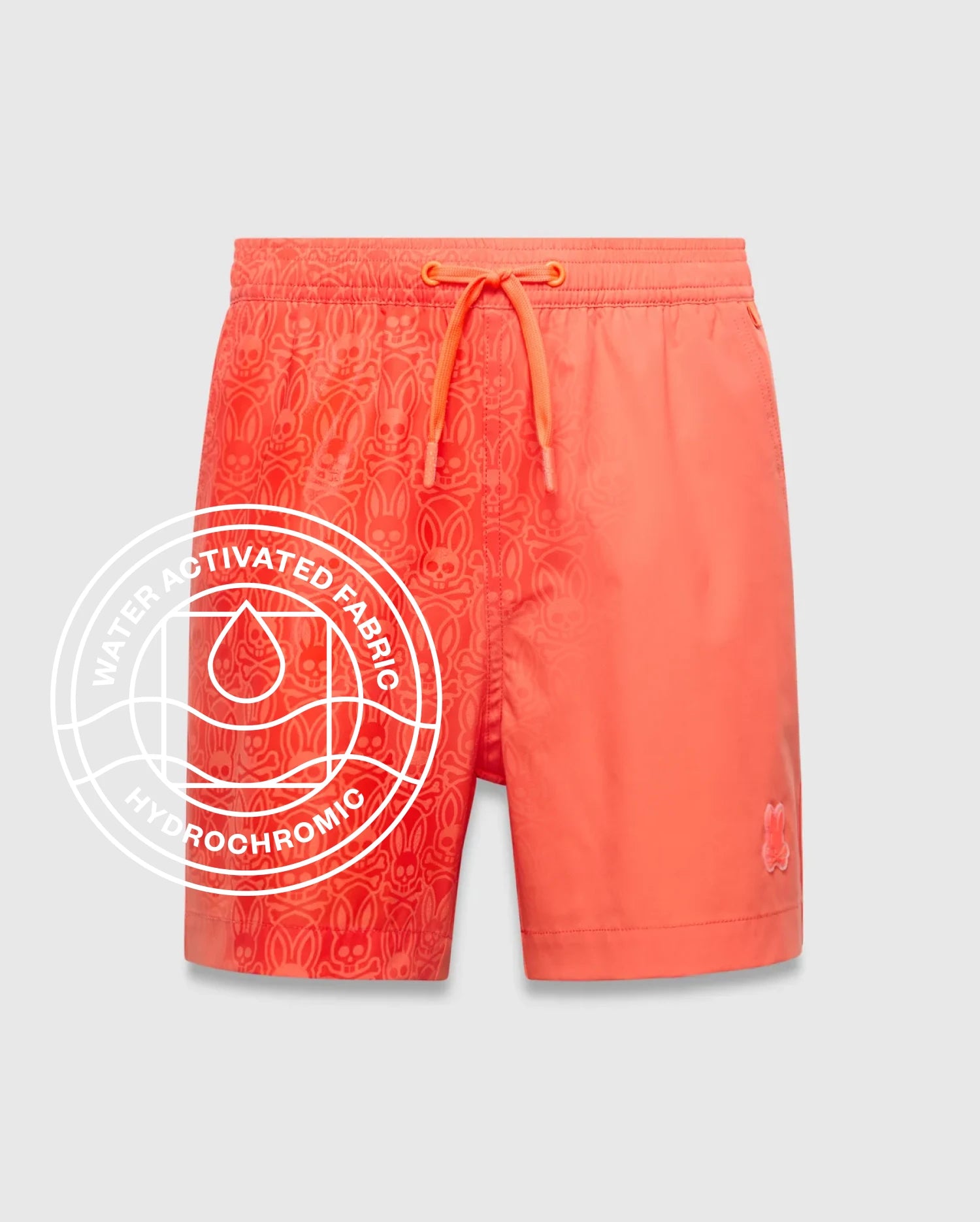 Kids Samos Hydrochromic Printed Swim Trunk in vibrant coral, featuring a water-activated all-over Psycho Bunny skull pattern on the left, solid right leg, and small embroidered bunny logo.