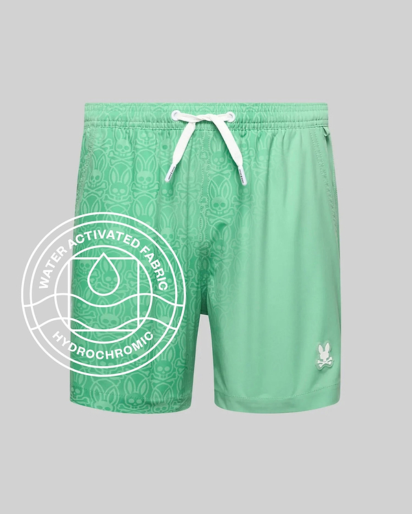 Kids Samos Hydrochromic Printed Swim Trunk in mint green, featuring a relaxed fit, white drawstrings, and a small white Psycho Bunny skull logo on the lower right leg. The smooth fabric reveals a tonal bunny skull pattern when wet.