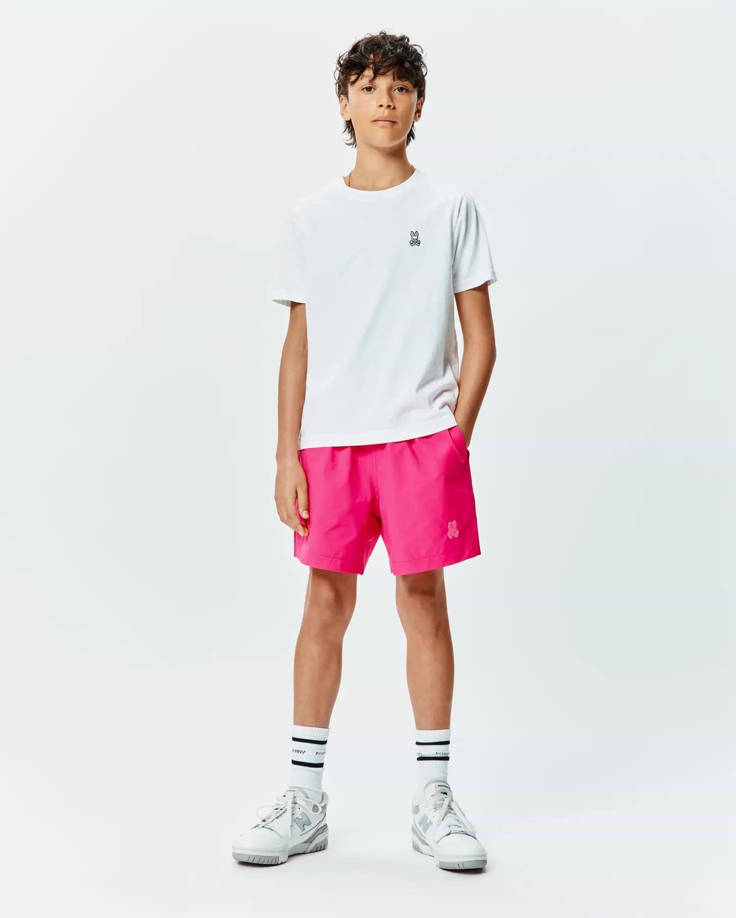 White classic-fit jersey t-shirt with small embroidered Psycho Bunny skull logo on chest, paired with hot pink Kids Samos Hydrochromic Printed Swim Trunk featuring a tonal embroidered bunny skull.