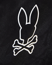 A black background features a white, minimalist graphic of a bunny head with long ears positioned above two crossed bones, resembling a skull and crossbones design on quick-dry material in the KIDS PARKER HYDROCHROMIC SWIM TRUNK - B0W646C200 from Psycho Bunny.