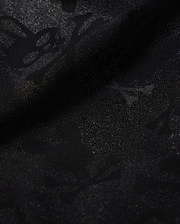 A detailed close-up of a Psycho Bunny KIDS PARKER HYDROCHROMIC SWIM TRUNK - B0W646C200 fabric displaying a subtle textured pattern with skull and crossbones and other abstract shapes. The slightly shiny, quick-dry material adds depth and dimension to the dark hydrochromatic pattern.