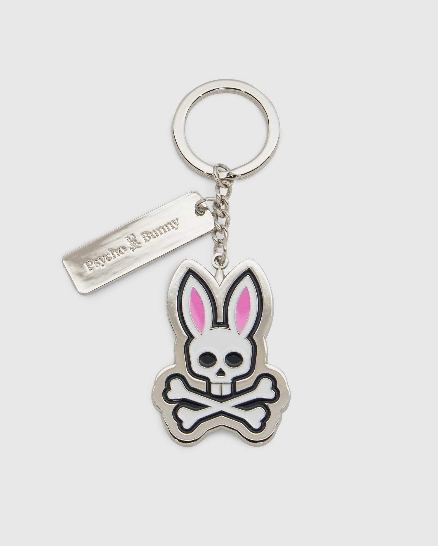 Introducing the CLASSIC BUNNY KEYCHAIN - B6A372E200 from Psycho Bunny, a fashionable metal accessory showcasing a cartoon bunny skull and crossbones design with distinctive pink ears. This practical everyday keychain features a sleek rectangular tag engraved with "Psycho Bunny." Complemented by a silver-colored chain and keyring, it adds a chic touch to your essentials.
