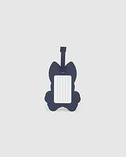 A navy blue luggage tag in the shape of a cat is pictured. The front side features a rectangular white label with blank lines for writing contact information. Made from detachable silicone, the Psycho Bunny MENS LUGGAGE TAG - B6A387B200 has a strap at the top for attaching to luggage.