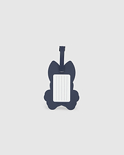 A navy blue luggage tag in the shape of a cat is pictured. The front side features a rectangular white label with blank lines for writing contact information. Made from detachable silicone, the Psycho Bunny MENS LUGGAGE TAG - B6A387B200 has a strap at the top for attaching to luggage.