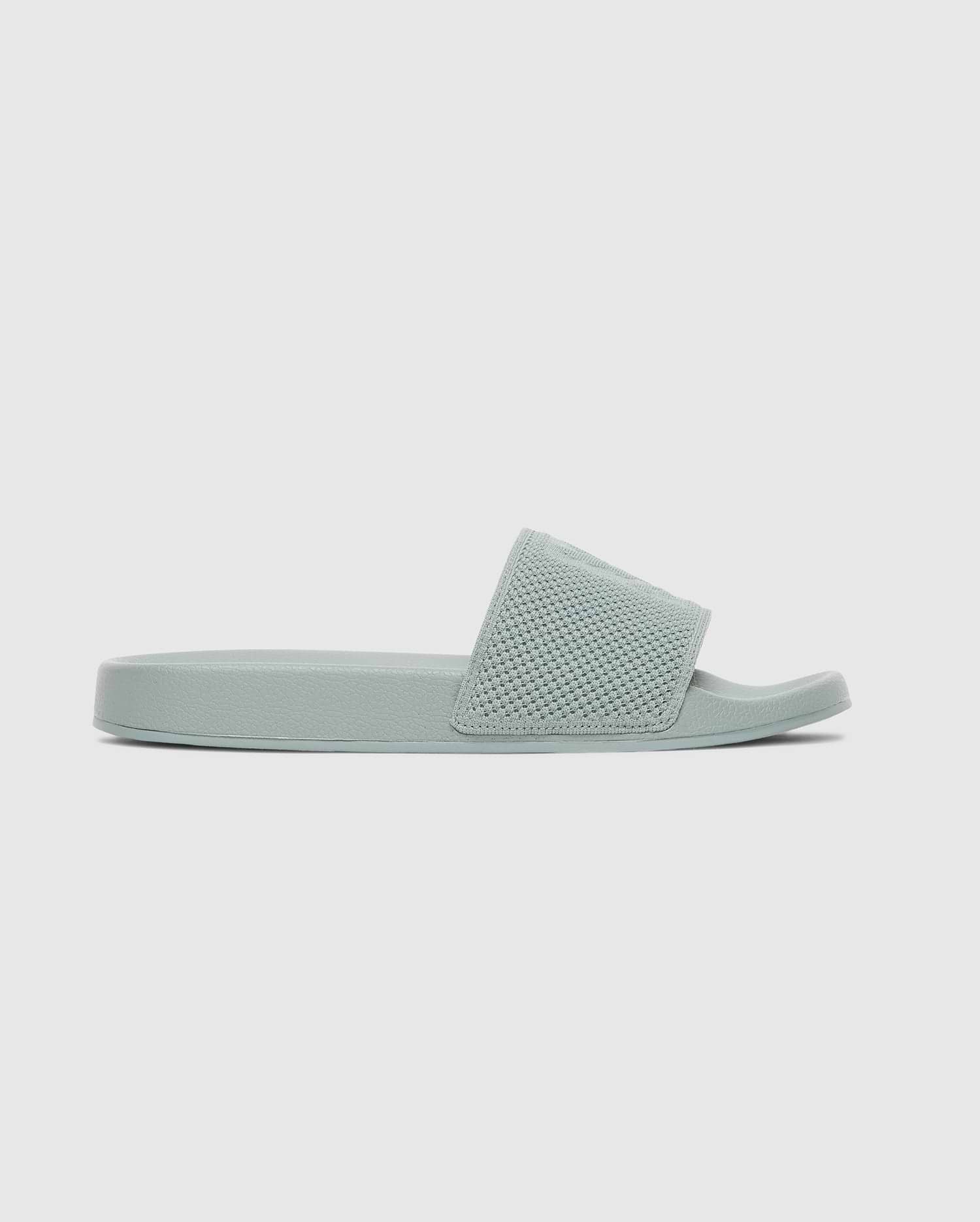 The Psycho Bunny MENS KNIT SLIDES - B6A474F200 feature a light green knit upper, textured wide strap, flat sole, and ergonomically molded footbed, shown in side profile against a plain light background.