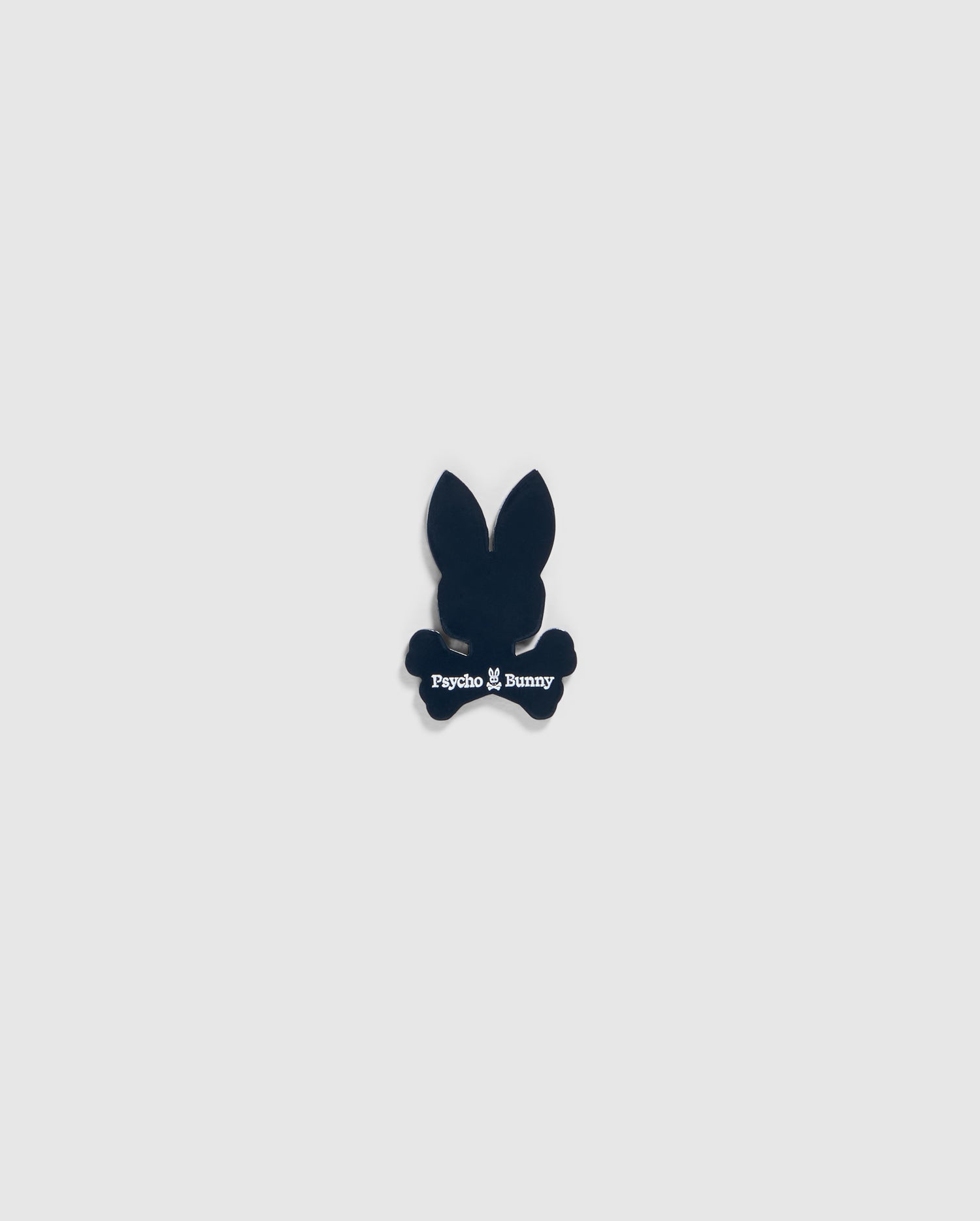 A small black silhouette of a bunny head with long ears and crossbones underneath, featuring the text "Psycho Bunny" in white below the head and above the crossbones, designed as an edgy BALL MARKER - B6A698C200 perfect for any golfer's collection by Psycho Bunny.