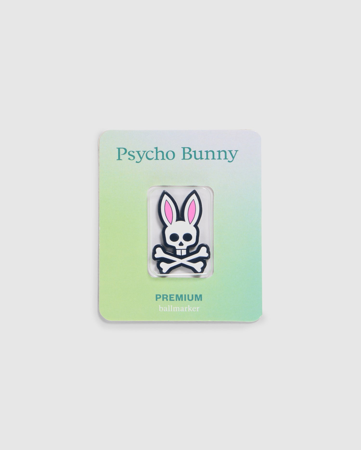 Explore the Psycho Bunny golfers collection with this premium ball marker featuring a white skull with pink bunny ears. Attached to a gradient card transitioning from light green to light blue, it showcases "Psycho Bunny" at the top and "PREMIUM BALL MARKER - B6A698C200" at the bottom.
