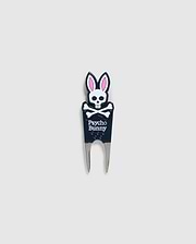 Image of a DIVOT TOOL - B6A699C200 from Psycho Bunny with a design featuring a skull with bunny ears and the text "Psycho Bunny" underneath. The tool has two prongs at the bottom, and the skull and ears are in black, white, and pink. A perfect addition to golf gifts, this tool also comes with a magnetic ball marker. The background is plain gray.