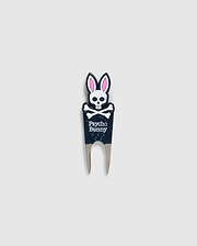 Image of a DIVOT TOOL - B6A699C200 from Psycho Bunny with a design featuring a skull with bunny ears and the text "Psycho Bunny" underneath. The tool has two prongs at the bottom, and the skull and ears are in black, white, and pink. A perfect addition to golf gifts, this tool also comes with a magnetic ball marker. The background is plain gray.