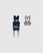 A DIVOT TOOL - B6A699C200 featuring a stylized bunny logo, perfect for golf gifts. The black divot tool sports the Psycho Bunny logo with a bunny head shape at the top. The magnetic ball marker showcases a bunny skull design with crossbones and pink ears, all set against a plain background.