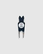 A Psycho Bunny DIVOT TOOL - B6A699C200 featuring a black handle with a white circular logo. The logo shows an illustration of a bunny head with crossed bones underneath. The two prongs of the tool are metal, and it includes a magnetic ball marker. Ideal for those seeking unique golf gifts.