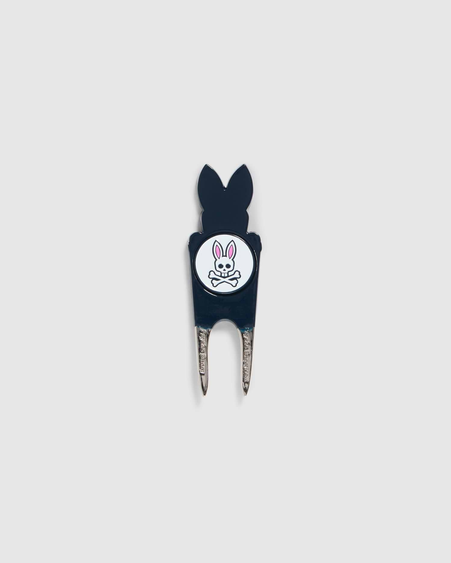 A Psycho Bunny DIVOT TOOL - B6A699C200 featuring a black handle with a white circular logo. The logo shows an illustration of a bunny head with crossed bones underneath. The two prongs of the tool are metal, and it includes a magnetic ball marker. Ideal for those seeking unique golf gifts.