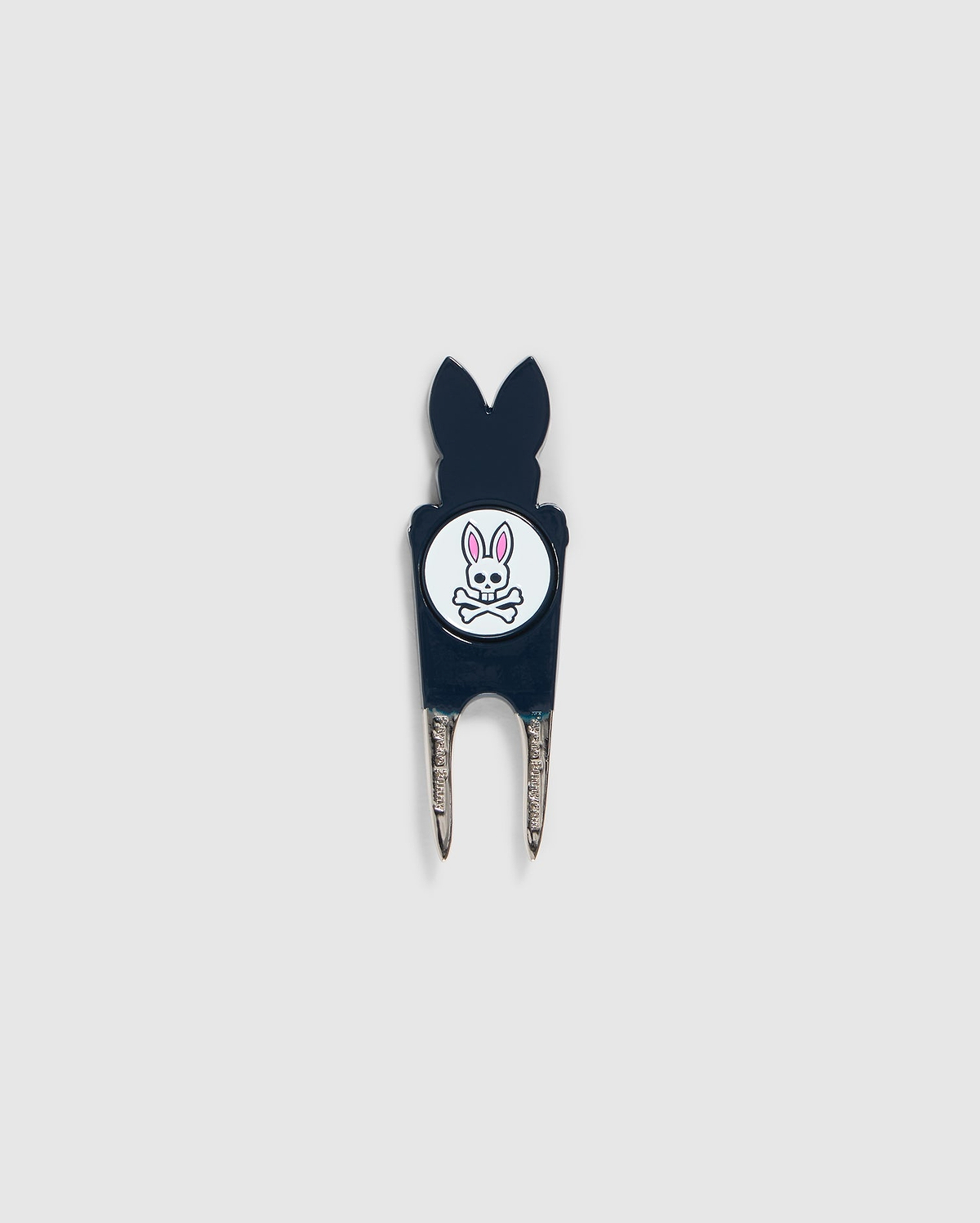 A Psycho Bunny DIVOT TOOL - B6A699C200 featuring a black handle with a white circular logo. The logo shows an illustration of a bunny head with crossed bones underneath. The two prongs of the tool are metal, and it includes a magnetic ball marker. Ideal for those seeking unique golf gifts.