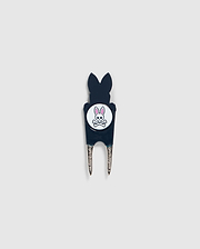 A Psycho Bunny DIVOT TOOL - B6A699C200 featuring a black handle with a white circular logo. The logo shows an illustration of a bunny head with crossed bones underneath. The two prongs of the tool are metal, and it includes a magnetic ball marker. Ideal for those seeking unique golf gifts.