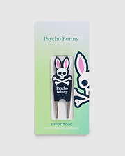 A Psycho Bunny branded DIVOT TOOL - B6A699C200 with a removable magnetic ball marker is displayed in its packaging. The tool features a bunny logo with crossbones and the text "Psycho Bunny" below it. The packaging has a green gradient background and a larger bunny logo on the right side, making it perfect for golf gifts.