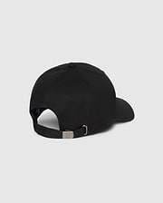 A Psycho Bunny MENS CLASSIC BASEBALL CAP - B6A816A1HT is shown from the back. The black cotton twill cap features an adjustable strap with a metal buckle and a small round vent hole on the side. The background is a plain grey.