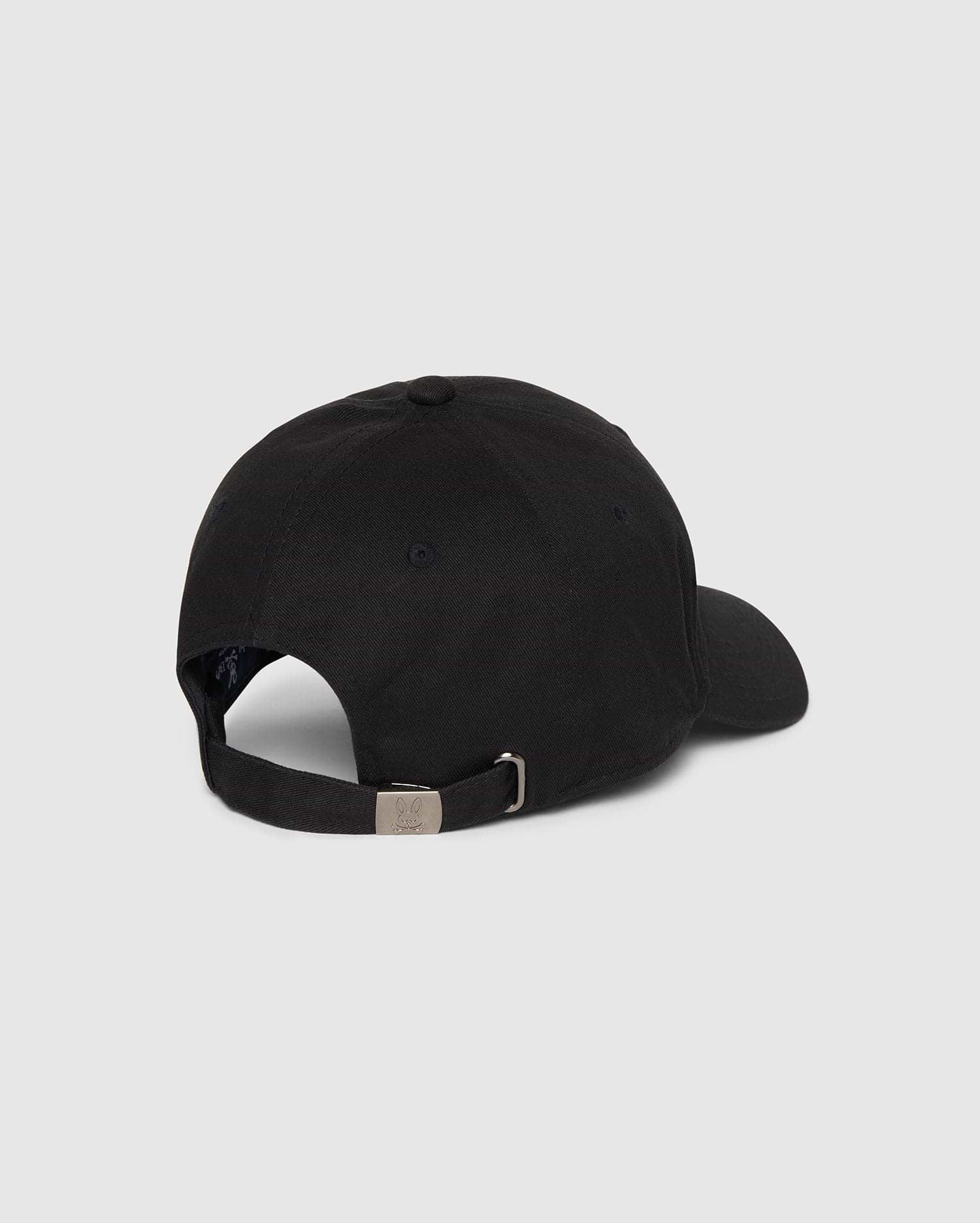A Psycho Bunny MENS CLASSIC BASEBALL CAP - B6A816A1HT is shown from the back. The black cotton twill cap features an adjustable strap with a metal buckle and a small round vent hole on the side. The background is a plain grey.