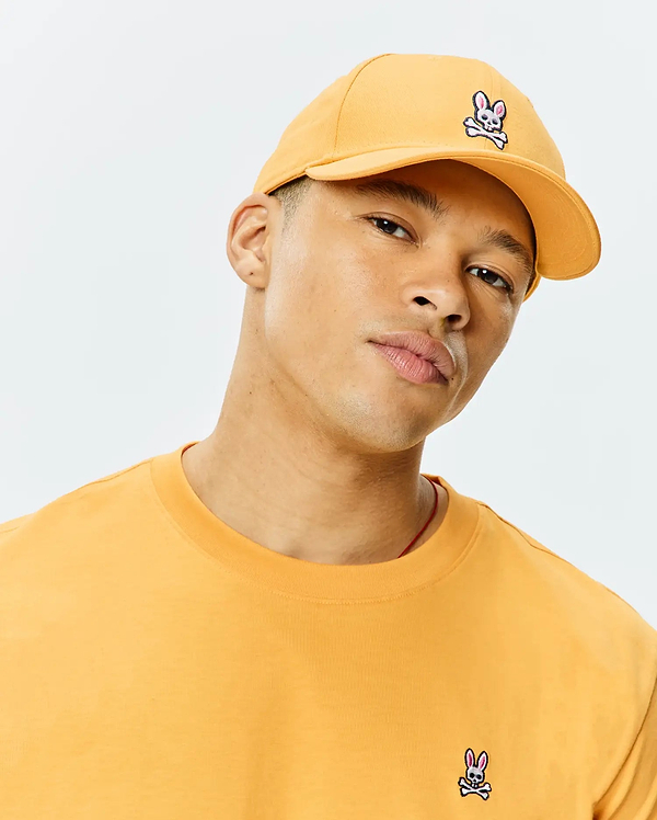 Mustard yellow Mens Classic Baseball Cap with embroidered Psycho Bunny skull logo on front, paired with a classic fit jersey t-shirt featuring a matching embroidered logo on the left chest.
