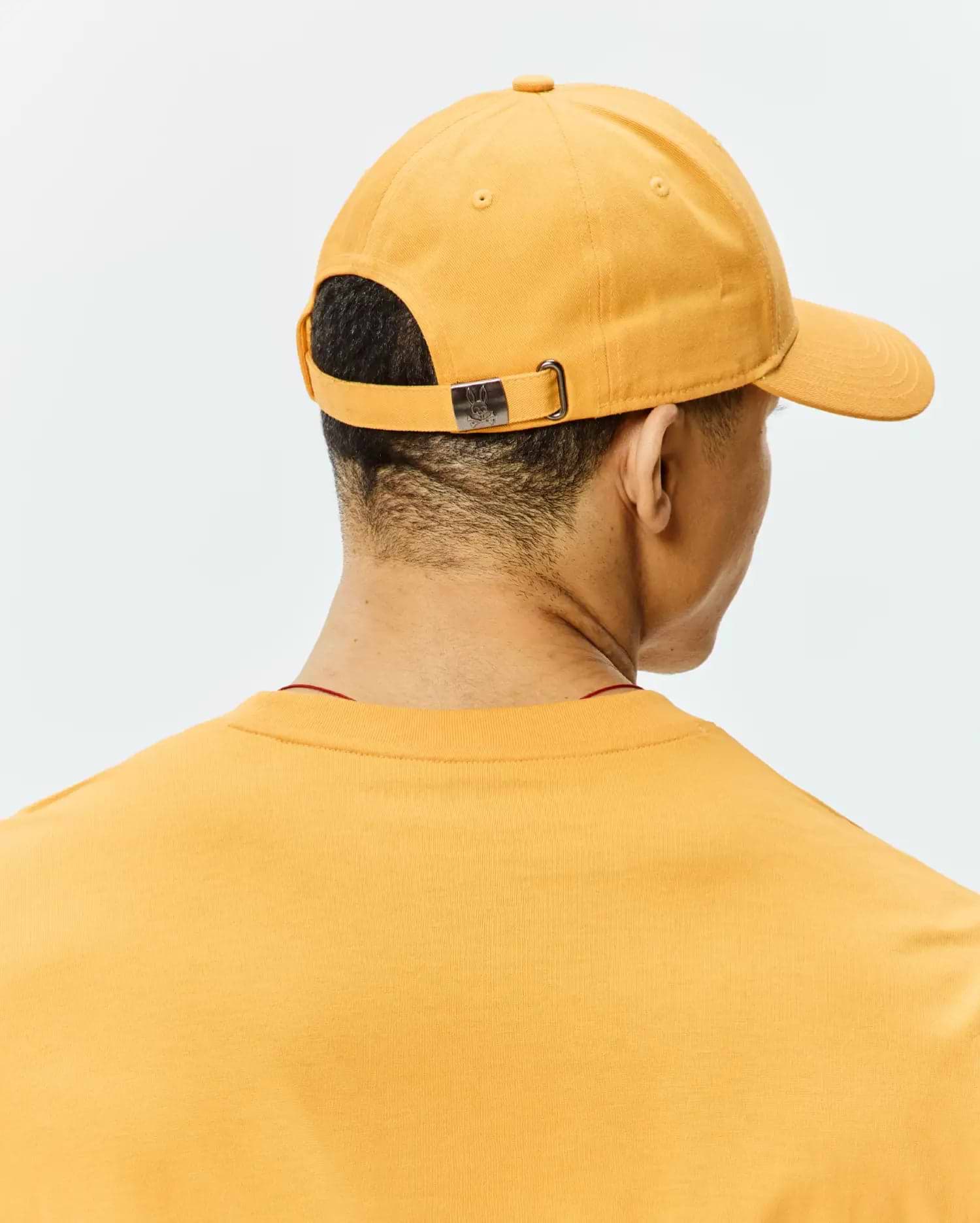 Golden Yellow Mens Classic Baseball Cap, cotton twill, with a metallic Psycho Bunny skull logo on the adjustable back buckle, and a matching jersey knit t-shirt with a subtle red collar.