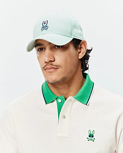 Off-white pique polo with bright green collar, navy stripe, and embroidered Psycho Bunny skull logo with sunglasses on chest. Light mint Mens Classic Baseball Cap with embroidered Psycho Bunny logo.