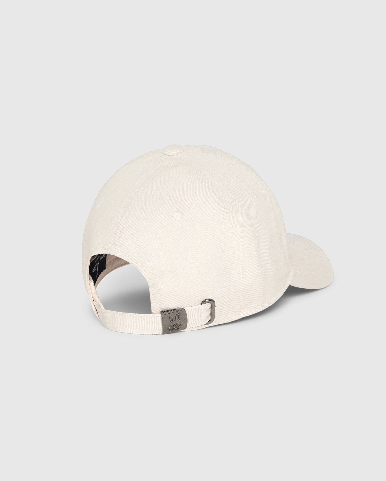 The MENS CLASSIC BASEBALL CAP - B6A816B200 by Psycho Bunny, crafted from 100% cotton in a classic beige shade, is displayed from the back against a plain light background. It boasts a curved brim, an adjustable strap with a metal clasp, and a side ventilation hole for enhanced comfort.