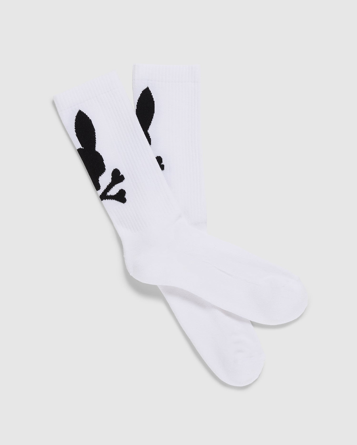 A pack of 3 Men's Sport Socks (B6F997D200) by Psycho Bunny, crafted from luxurious Peruvian Pima cotton in white, features a distinctive black graphic design of a skull with bunny ears and bones. The socks are displayed with one pair slightly overlapping the other on a plain, light-colored background.