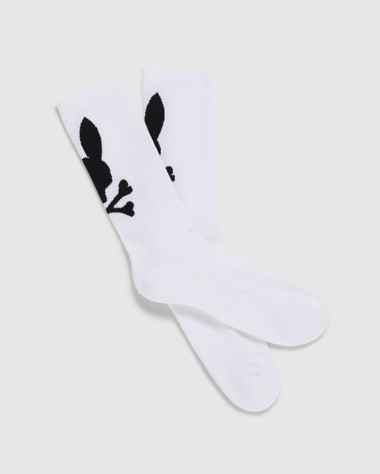 A pack of 3 Men's Sport Socks (B6F997D200) by Psycho Bunny, crafted from luxurious Peruvian Pima cotton in white, features a distinctive black graphic design of a skull with bunny ears and bones. The socks are displayed with one pair slightly overlapping the other on a plain, light-colored background.