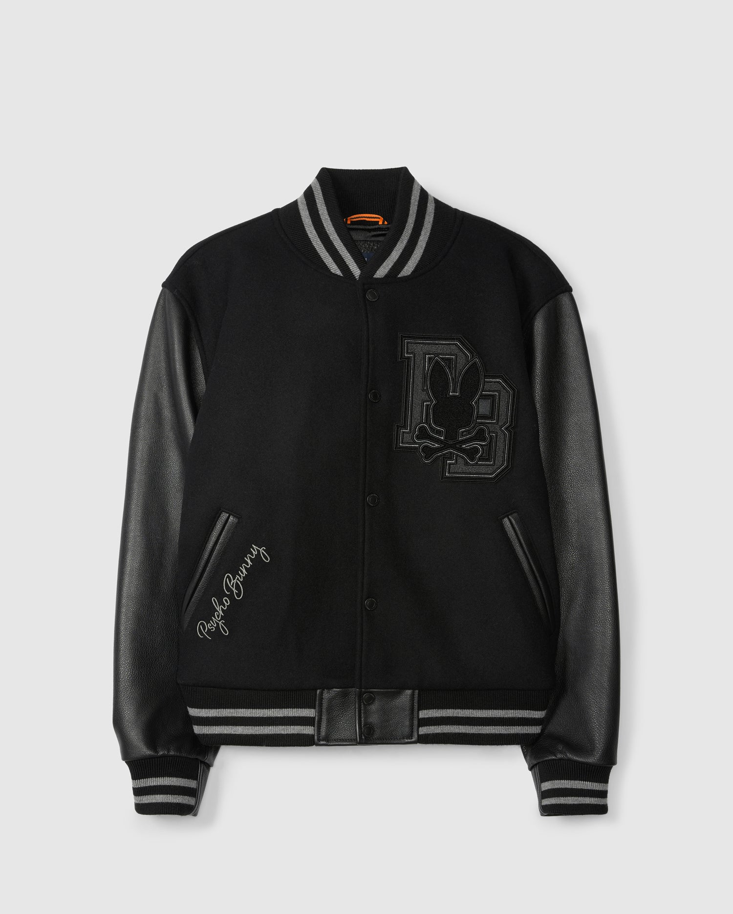 Presenting the Psycho Bunny Men's Brayden Wool Leather Varsity Bomber (B6J876D200): a sleek black jacket featuring eye-catching leather sleeves, striped cuffs, and a striking embroidered patch on the chest with initials and a rabbit silhouette. The phrase "Playboy Bunny" is elegantly stitched near the pocket for added flair.