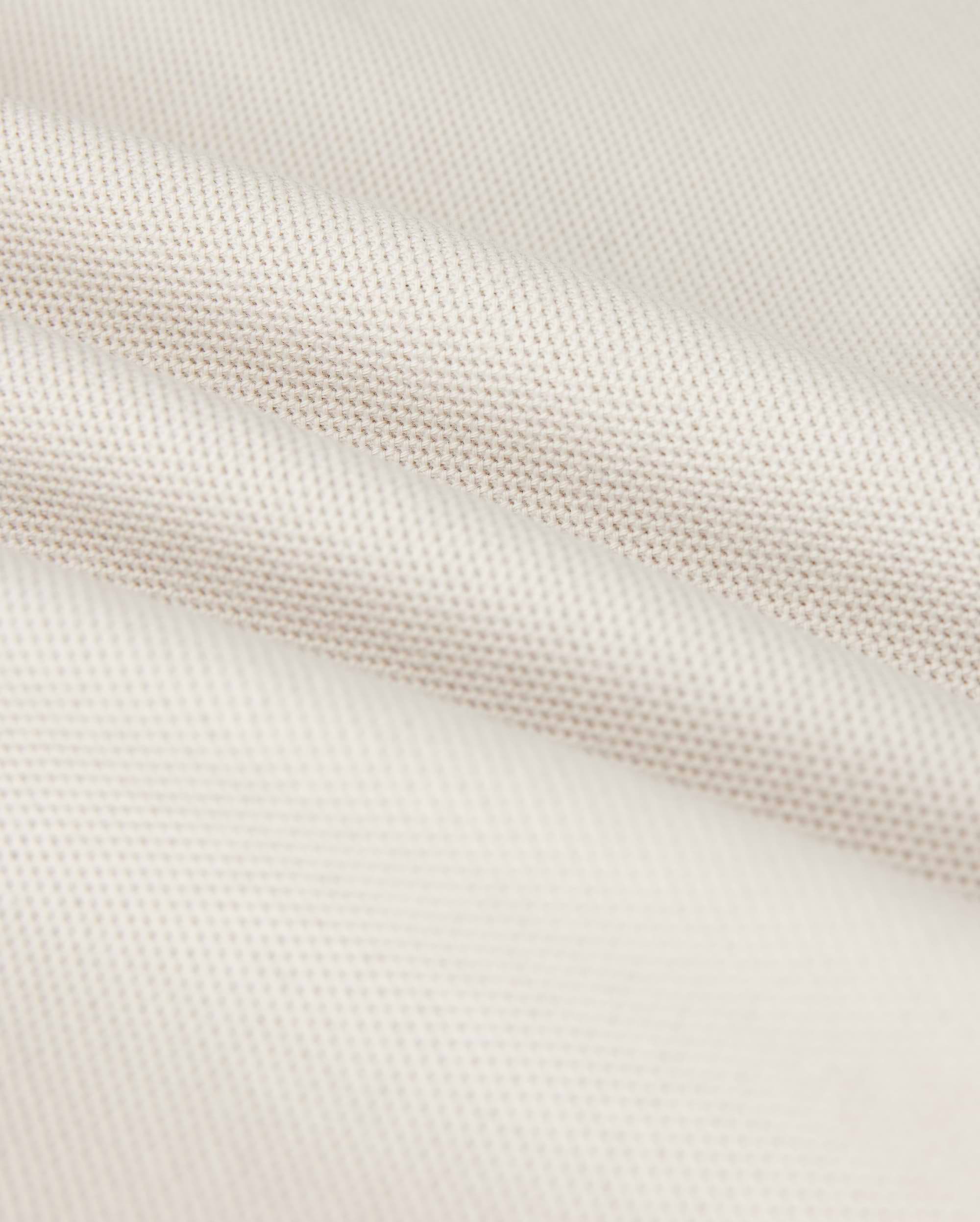 Close-up of a softly folded, light beige textured fabric with a subtle grid pattern, showcasing its smooth and pliable nature. The gentle folds add depth and highlight the luxurious Pima cotton's fine weave and soft sheen, hinting at the perfect fit for a Psycho Bunny Men's Classic Pique Polo Shirt - B6K001B200.