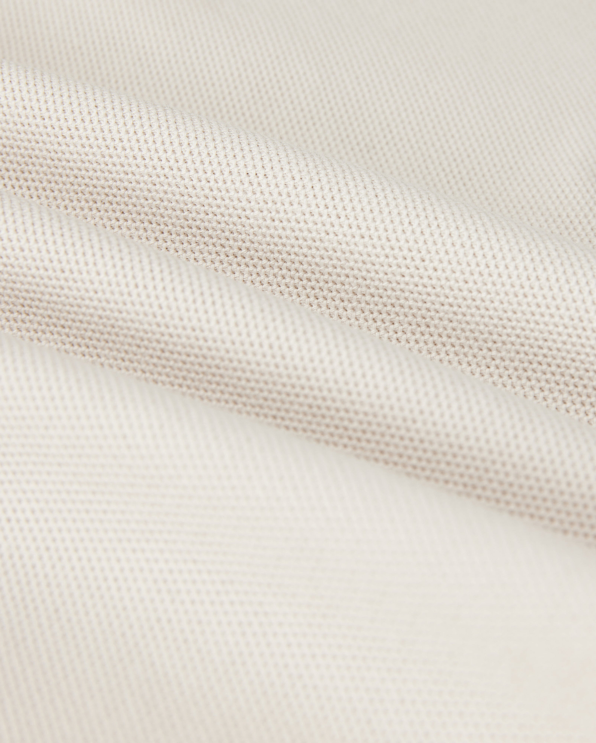 Close-up of a softly folded, light beige textured fabric with a subtle grid pattern, showcasing its smooth and pliable nature. The gentle folds add depth and highlight the luxurious Pima cotton's fine weave and soft sheen, hinting at the perfect fit for a Psycho Bunny Men's Classic Pique Polo Shirt - B6K001B200.