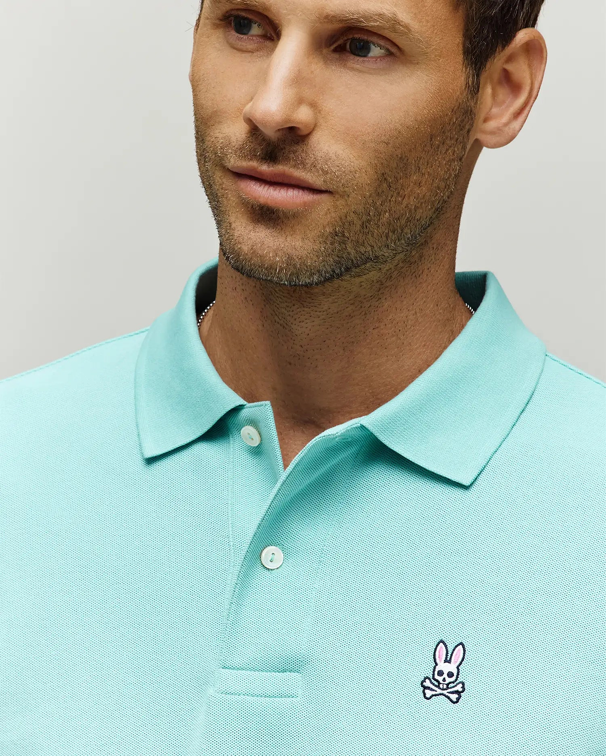 Mens Classic Pique Polo in aqua, featuring a classic fit, textured pique knit fabric, two-button placket, and a small embroidered pink and white Psycho Bunny skull logo on the left chest.