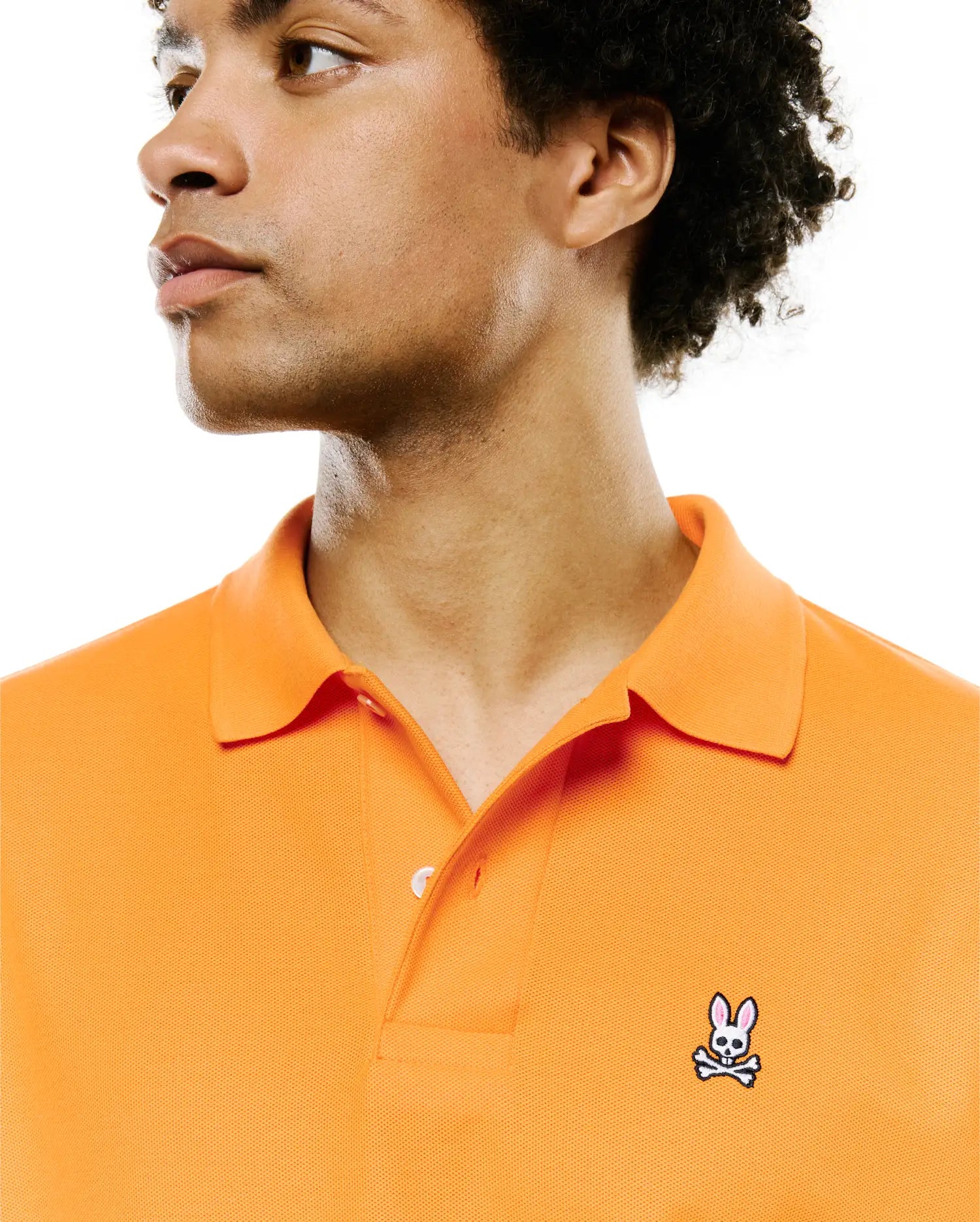 Mens Classic Pique Polo in vibrant orange, featuring a textured pique fabric, two-button placket, and a small, embroidered Psycho Bunny skull logo on the left chest.