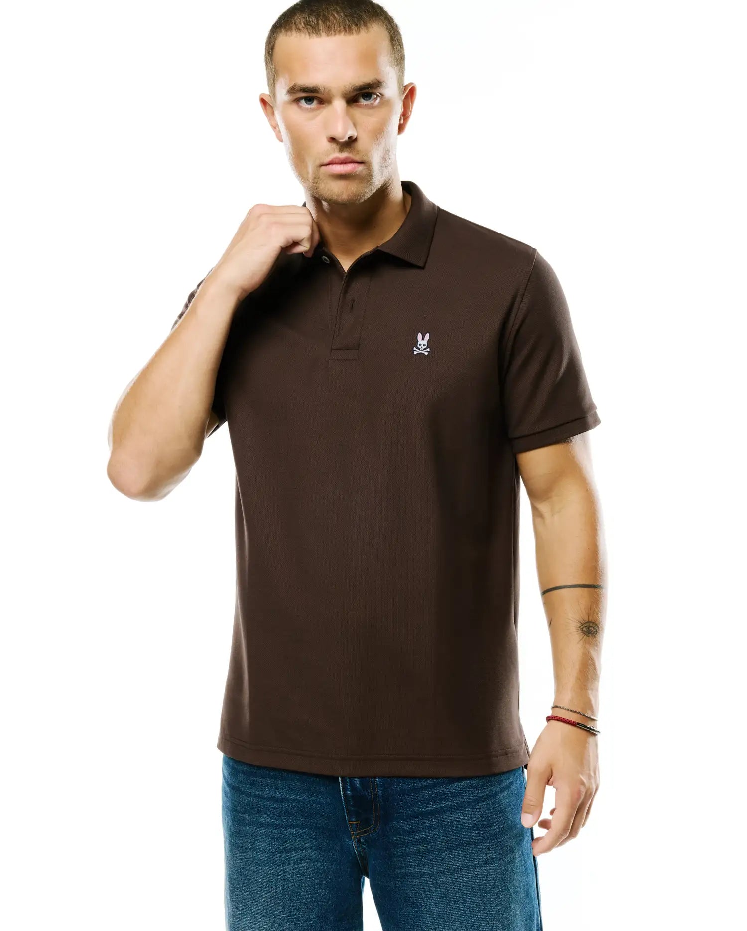 Men's Classic Pima Pique Polo in rich brown pique fabric, featuring a small, embroidered white Psycho Bunny skull logo on the left chest, with a classic fit. (2)