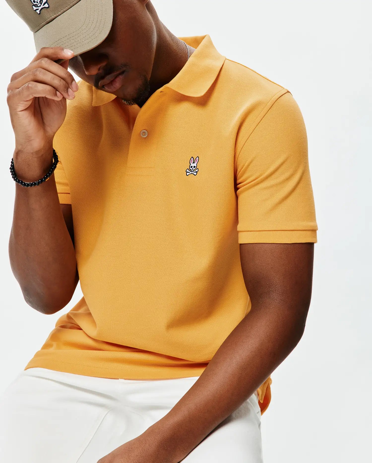 Mens Classic Pique Polo in marigold orange, featuring a classic fit, textured pique fabric, two-button placket, and a small embroidered Psycho Bunny skull logo on the left chest.