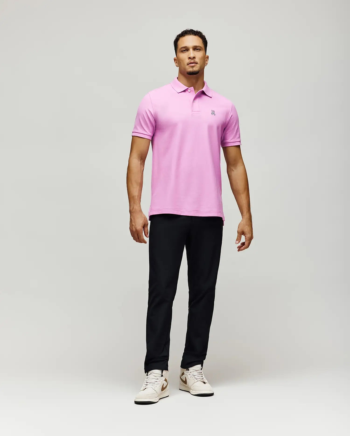 Mens Classic Pique Polo, a vibrant pink classic fit polo shirt crafted from textured pique fabric, featuring a small, intricately embroidered Psycho Bunny skull logo on the left chest.