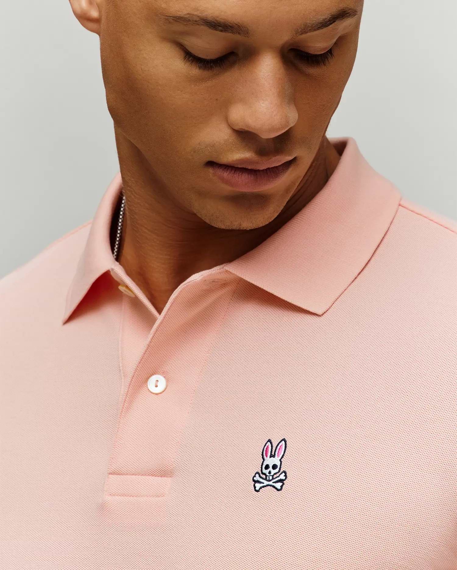 Mens Classic Pique Polo in pink, featuring a classic fit, pique knit texture, two-button placket with white buttons, and a small embroidered Psycho Bunny skull logo on the left chest.