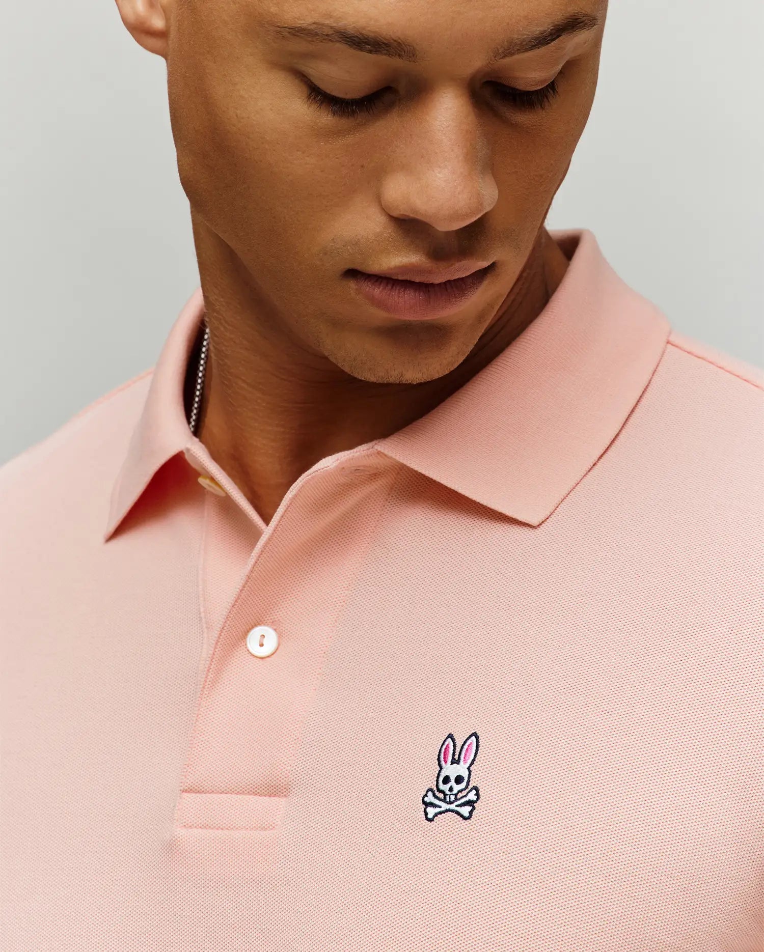 Mens Classic Pique Polo in pink, featuring a classic fit, pique knit texture, two-button placket with white buttons, and a small embroidered Psycho Bunny skull logo on the left chest.