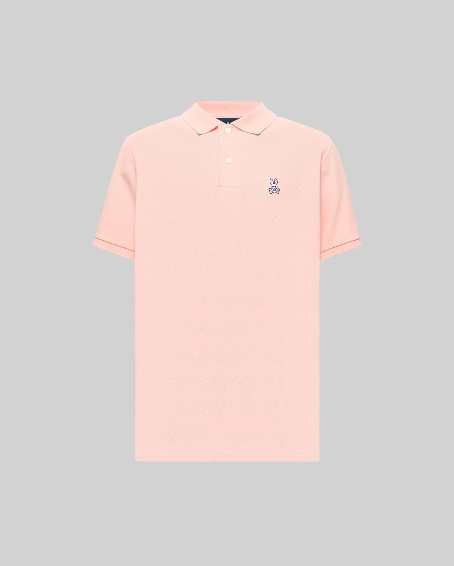 Mens Classic Pique Polo in peach, featuring a classic fit, pique knit texture, two-button placket, and a small embroidered purple, white, and black Psycho Bunny skull logo on the left chest with subtle red cuff tipping.