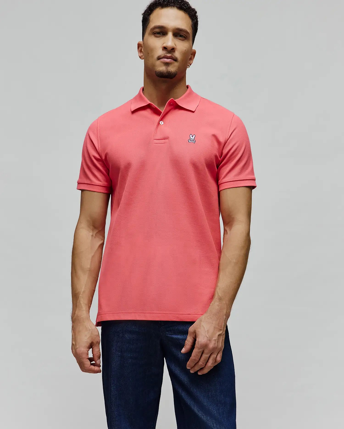 Mens Classic Pique Polo in vibrant coral pique knit, featuring a classic fit, two-button placket, and a small embroidered white Psycho Bunny skull logo on the left chest.