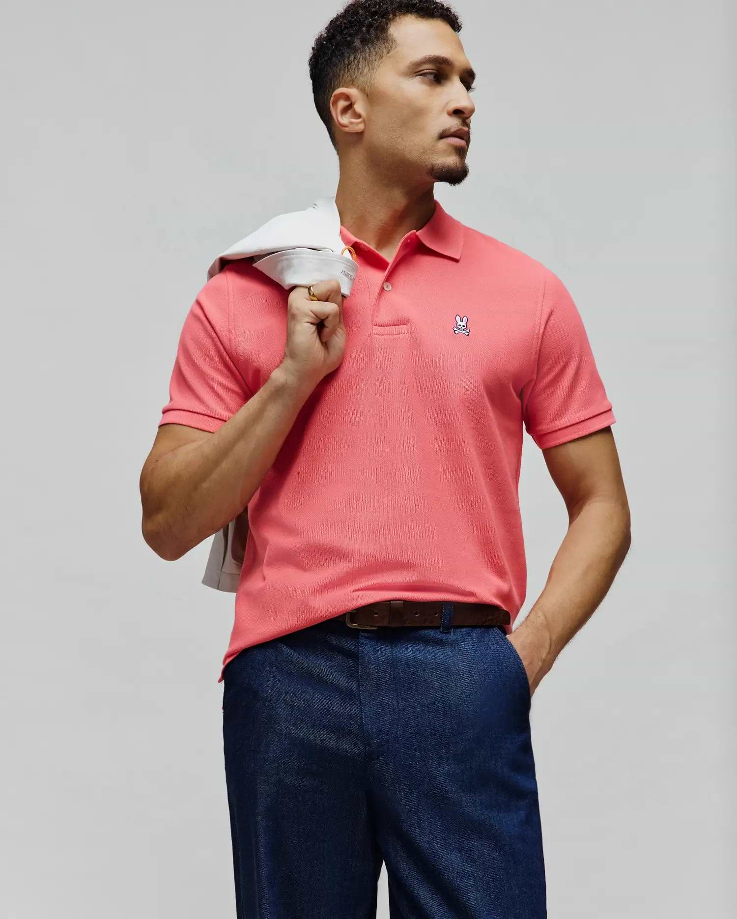 Mens Classic Pique Polo in vibrant coral pink, featuring a classic fit, two-button placket, and a small embroidered white Psycho Bunny skull logo with pink and black details on the left chest.