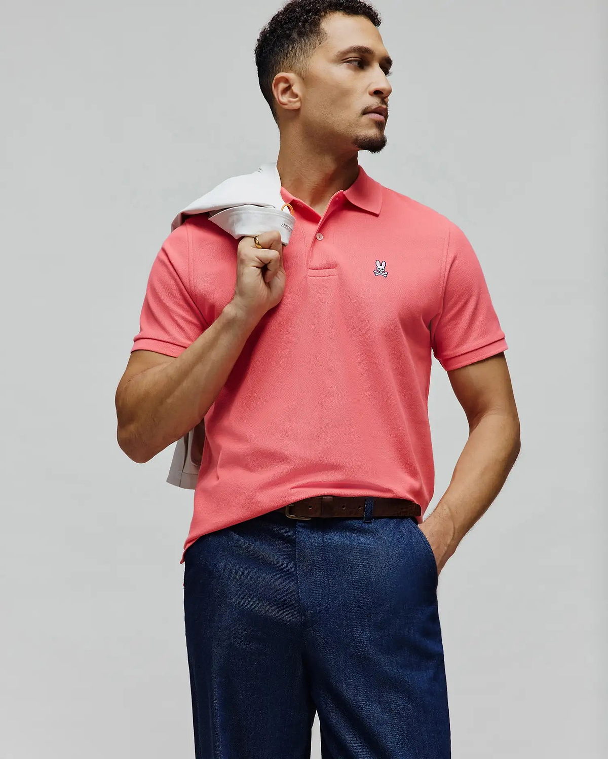 Mens Classic Pique Polo in vibrant coral pink, featuring a classic fit, two-button placket, and a small embroidered white Psycho Bunny skull logo with pink and black details on the left chest.