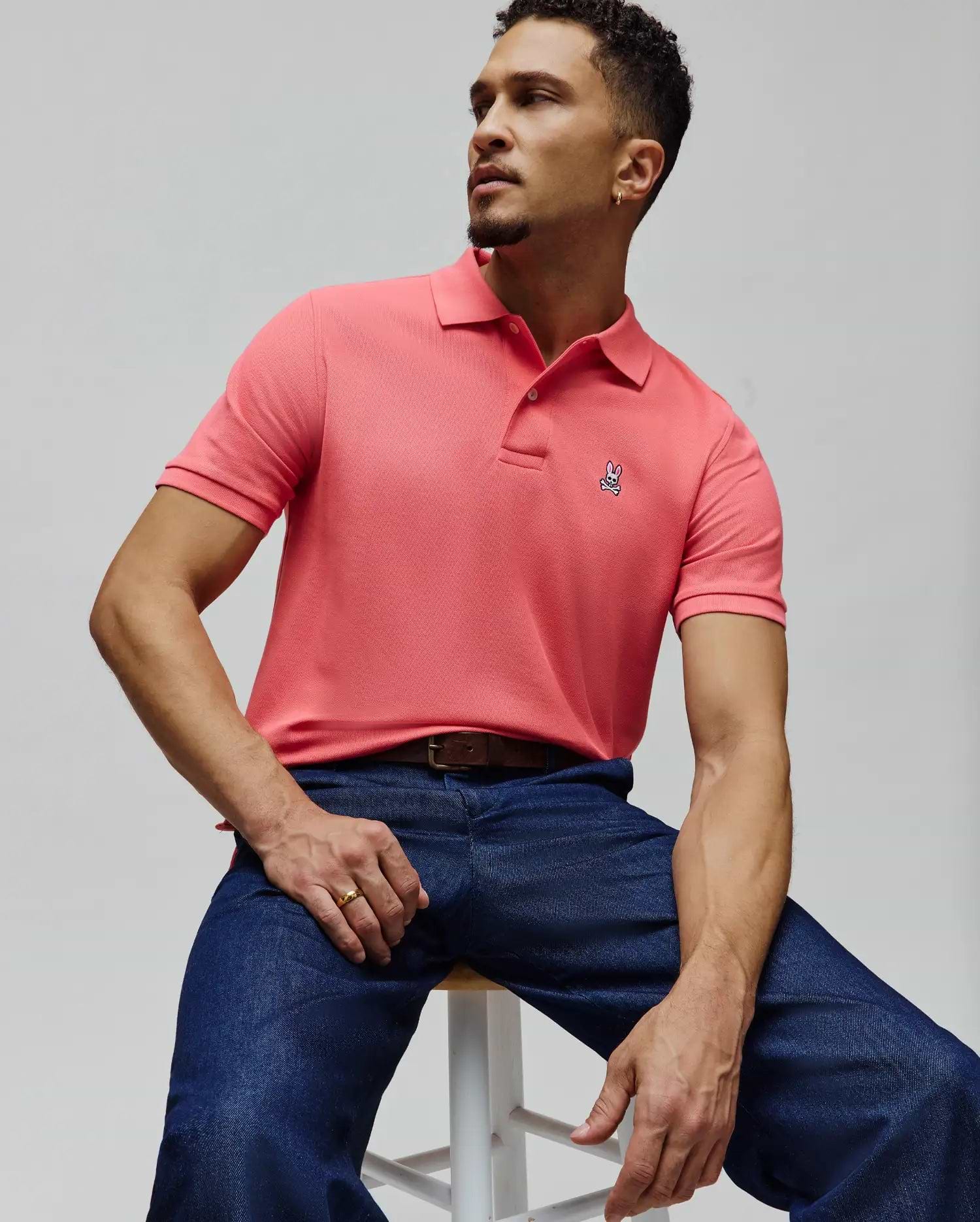 Mens Classic Pique Polo in vibrant coral, featuring a textured pique knit, classic fit, and a small, embroidered Psycho Bunny skull logo on the left chest.