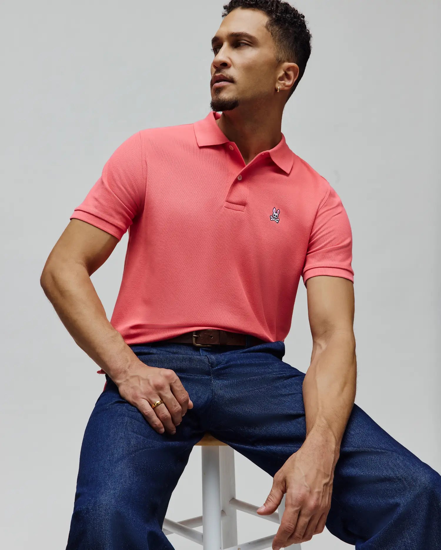 Mens Classic Pique Polo in vibrant coral, featuring a textured pique knit, classic fit, and a small, embroidered Psycho Bunny skull logo on the left chest.