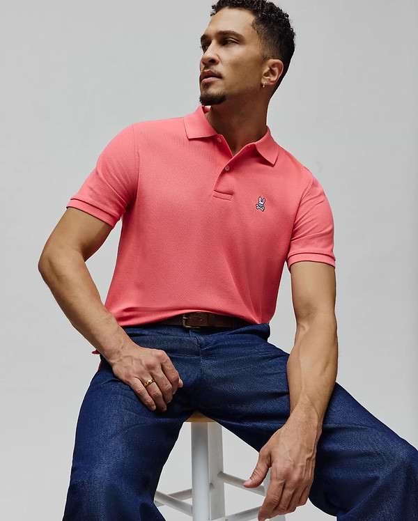 Mens Classic Pique Polo in vibrant coral, featuring a textured pique knit, classic fit, and a small, embroidered Psycho Bunny skull logo on the left chest.