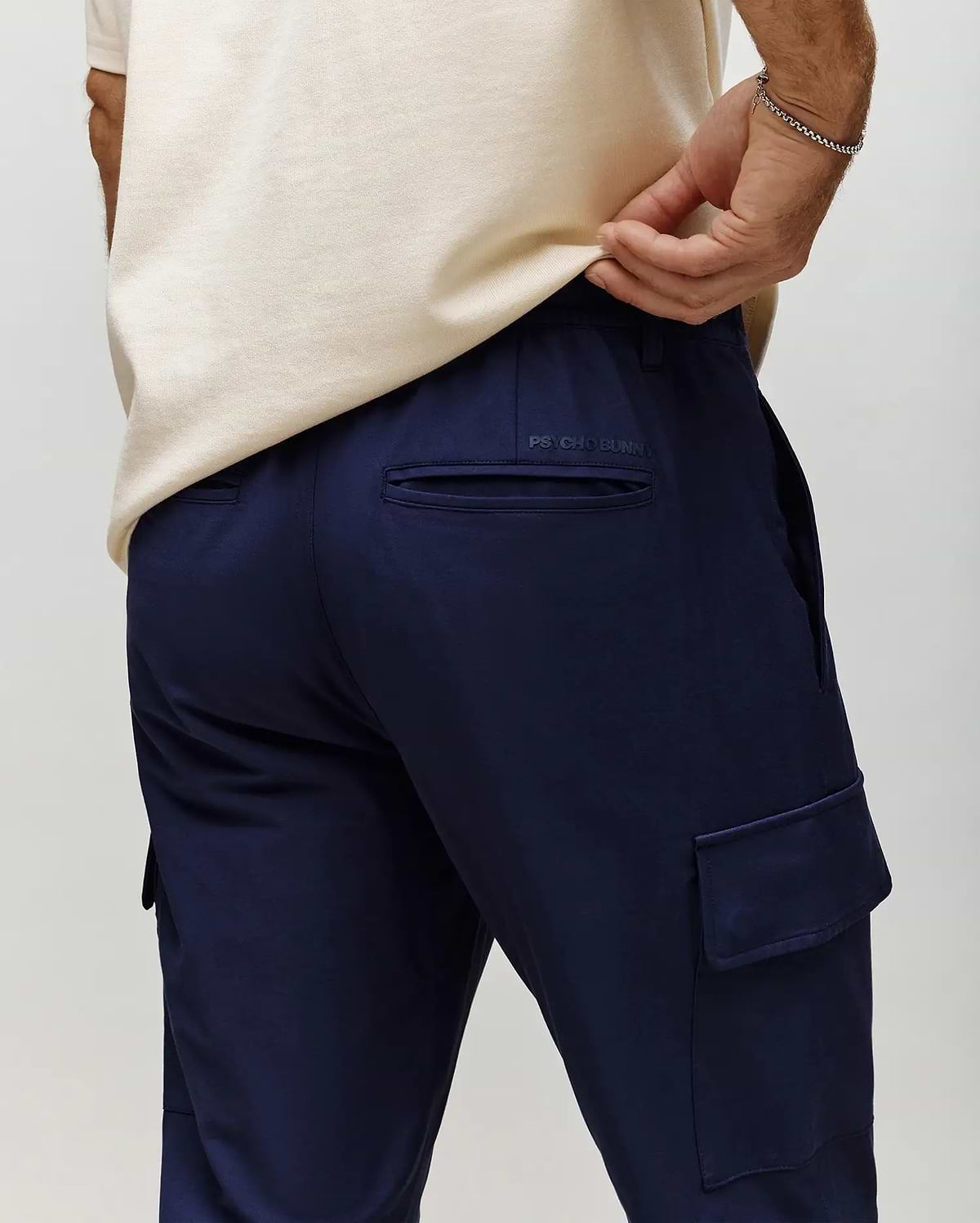 Mens Lloyd Cargo Jogger in navy, featuring a relaxed fit, smooth fabric, side cargo pockets, back welt pockets, and a subtle tonal Psycho Bunny text logo above the right back pocket.