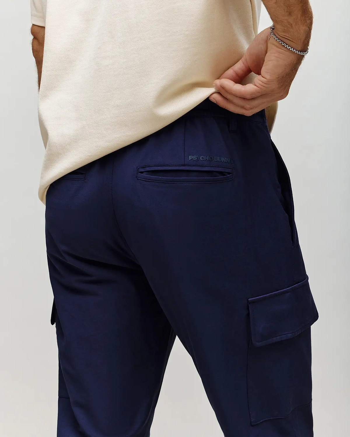 Mens Lloyd Cargo Jogger in navy, featuring a relaxed fit, smooth fabric, side cargo pockets, back welt pockets, and a subtle tonal Psycho Bunny text logo above the right back pocket.