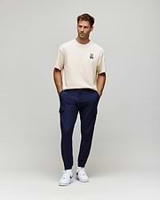 Ecru relaxed fit jersey t-shirt with a small embroidered Psycho Bunny skull logo on the left chest, paired with slim navy Mens Lloyd Cargo Jogger pants featuring cargo pockets and a white drawstring.