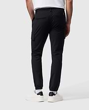 A person wearing Psycho Bunny's MENS LLOYD CARGO JOGGER - B6P159B200 in black, featuring elasticized cuffs and utilitarian pockets, paired with a white T-shirt, white socks, and white sneakers. The person is standing with their back facing the camera against a plain gray background.