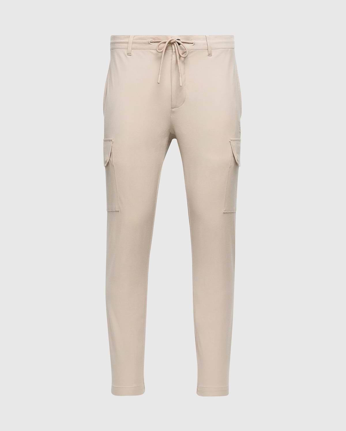 The MENS LLOYD CARGO JOGGER - B6P159B200 by Psycho Bunny is a pair of slim-fit beige cargo jogger pants, featuring tapered legs, an elastic waistband with a drawstring, two side pockets, and two cargo pockets on the thighs. These joggers are adorned with a subtle silicone branded detail.