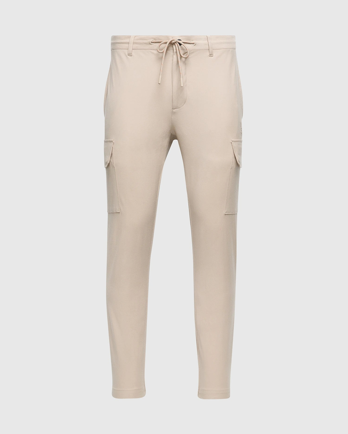 The MENS LLOYD CARGO JOGGER - B6P159B200 by Psycho Bunny is a pair of slim-fit beige cargo jogger pants, featuring tapered legs, an elastic waistband with a drawstring, two side pockets, and two cargo pockets on the thighs. These joggers are adorned with a subtle silicone branded detail.